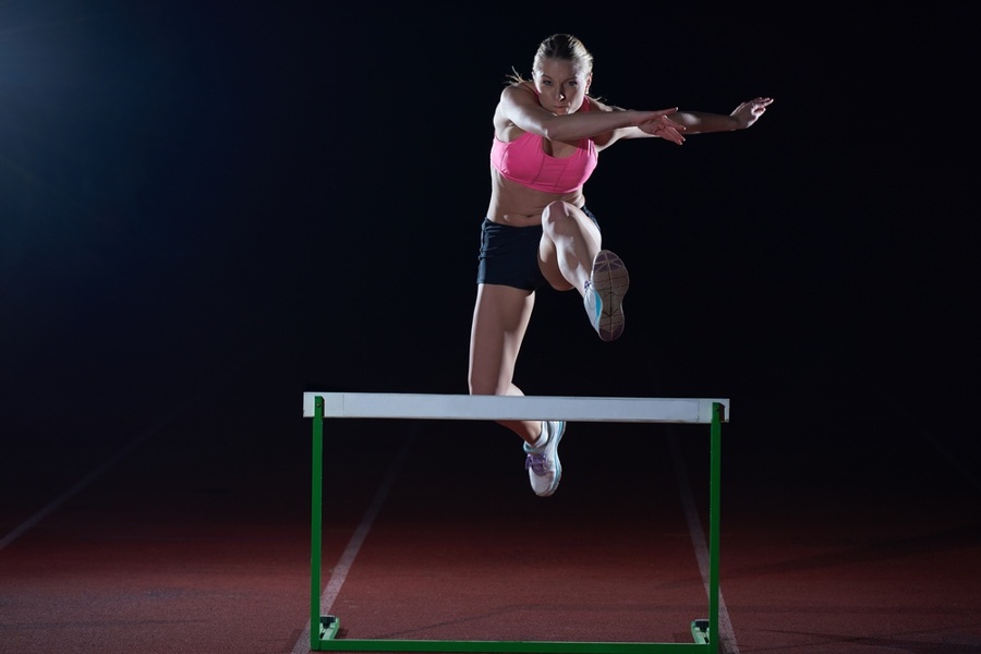 Determined young woman athlete jumping over a hurdles.jpeg